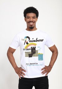 Vit bomullströja med en grafisk design av ett slott vid vattnet, med en regnbåge och texten "Regnbågen till Europa" i kraftfulla färger.