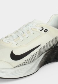 Λευκό αθλητικό παπούτσι με μαύρο λογότυπο Nike, λευκά κορδόνια και υφασμένο ασπρόμαυρο πάτο, εμφανιζόμενο σε κοντινή λήψη.