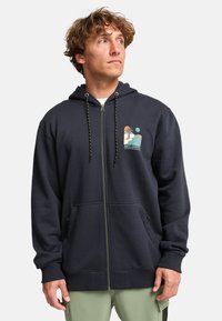 Sudadera con cremallera en color navy, hecha de forro polar, con un estampado gráfico en el pecho, capucha con cordón y bolsillos frontales. Cuenta con puños y dobladillo de canalé.