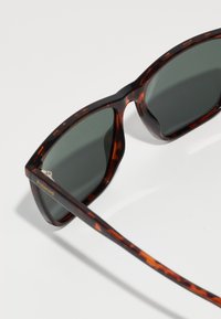 Ochelari de soare cu model țestoasă, având lentile de culoare gri închis, cu o ramă groasă și o textură netedă. Accentuati cu un mic logo Polaroid pe braț.