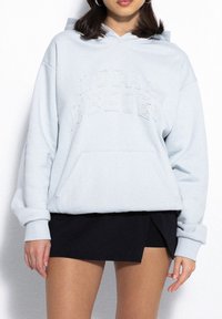 Jasnoniebieska bawełniana bluza z kapturem z napisem "LOKALNI BOHATEROWIE" w wypukłym haftem, z przednią kieszenią i swobodnym krojem.