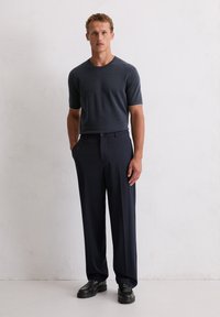 Czarnoszary sweter krótki z rękawami z zielonym wykończeniem, zestawiony z granatowymi spodniami i czarnymi mokasynami. Gładka tekstura, dopasowany krój, proste nogawki.