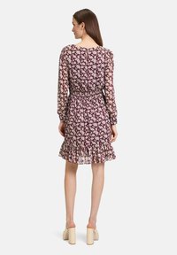Blumenmuster-Kleid mit geraffter Taille, langen Ärmeln und Rüschensaum. Hauptfarbe ist Burgundy mit cremefarbenen Akzenten. Rückseitiger Schlüsselloch-Ausschnitt sichtbar.