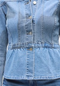 Φωτεινό γαλάζιο τζιν μπουφάν με εφαρμοστή μέση, κουμπιά μπροστά και πιέτα πεπλούμ στο κάτω μέρος. Υφή υφάσματος με ορατές λεπτομέρειες ραφής.