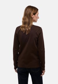 Chemise marron à manches longues en tissu doux, au design simple et à coupe droite. La vue arrière montre un col rond et une texture lisse.