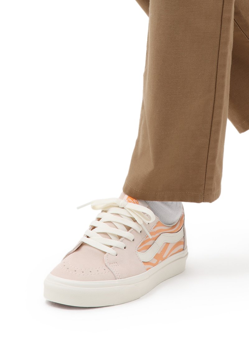Sneakers din suede roz deschis au șireturi albe și un model de valuri portocalii pe lateral. Talpa din cauciuc este, de asemenea, albă, cu accente bej.