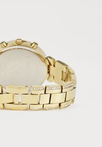 Gold metal watch with a linked bracelet, featuring decorative elements of small clear gemstones and a round case with multiple crowns.