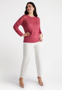 Top a maniche lunghe, in maglia rosa con righe orizzontali, abbinato a pantaloni bianchi a gamba dritta e scarpe con tacco trasparente. Tessuto morbido e vestibilità rilassata.