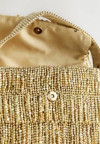 Goldene Taschenhandtasche mit einem seidenen Innenraum, ausgestattet mit einem Druckverschluss und einer strukturierten Oberfläche aus kleinen, reflektierenden Perlen.