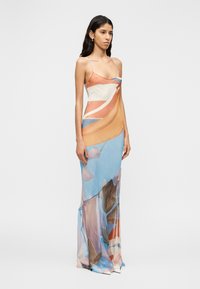 Μάξι φόρεμα με ελαφρύ, διαφανές υλικό με αφηρημένο μοτίβο σε πορτοκαλί, μπλε και καφέ χρώματα· λεπτές τιράντες και ρέουσα σιλουέτα.