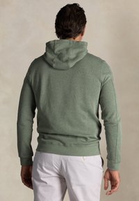 Groene hoodie van een textuurstof met een getailleerd ontwerp, voorzien van een capuchon met trekkoord en geribde manchetten, gecombineerd met lichte broeken.