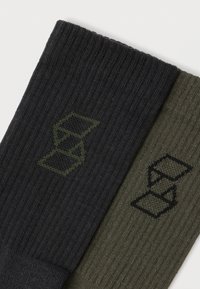 Κάλτσες από μείγμα βαμβακιού σε σκούρο γκρι και ελιά πράσινο, με ριμπ ύφη και αντίθετα λογότυπα σε γεωμετρικό σχέδιο σε κάθε κάλτσα.
