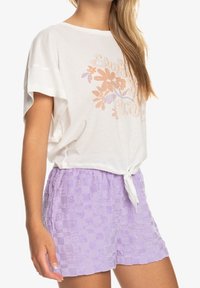 Weißes Baumwoll-T-Shirt mit floralem Grafikdesign in hellem Pfirsich und Lila; kombiniert mit sanften lavendelfarbenen karierter Shorts mit gebundenem Bund.