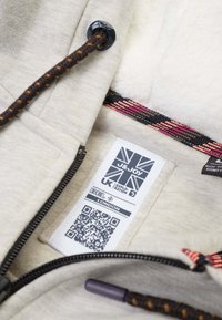 Lichtgrijze hoodie met een textuur aan de binnenkant, voorzien van een ritssluiting en een bruine gevlochten trekkoord, evenals een opvallend label en QR-code aan de binnenkant.