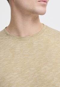 Tricou bej din bumbac texturat, cu decolteu rotund și dungi orizontale subtile, care evidențiază un material moale și ușor.