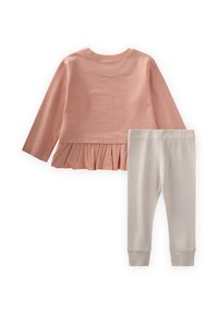 Różowa bluzka z długim rękawem i falbaniastym dołem oraz kremowe legginsy z prążkowanego materiału. Miękki, lekki bawełniany materiał. Elastyczny pasek w spodniach.