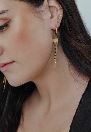 Goldene Ohrringe in Herzform mit Kettenakzenten und schwarzen Perlen, die detaillierte Verzierungen und ein glänzendes Finish zeigen.