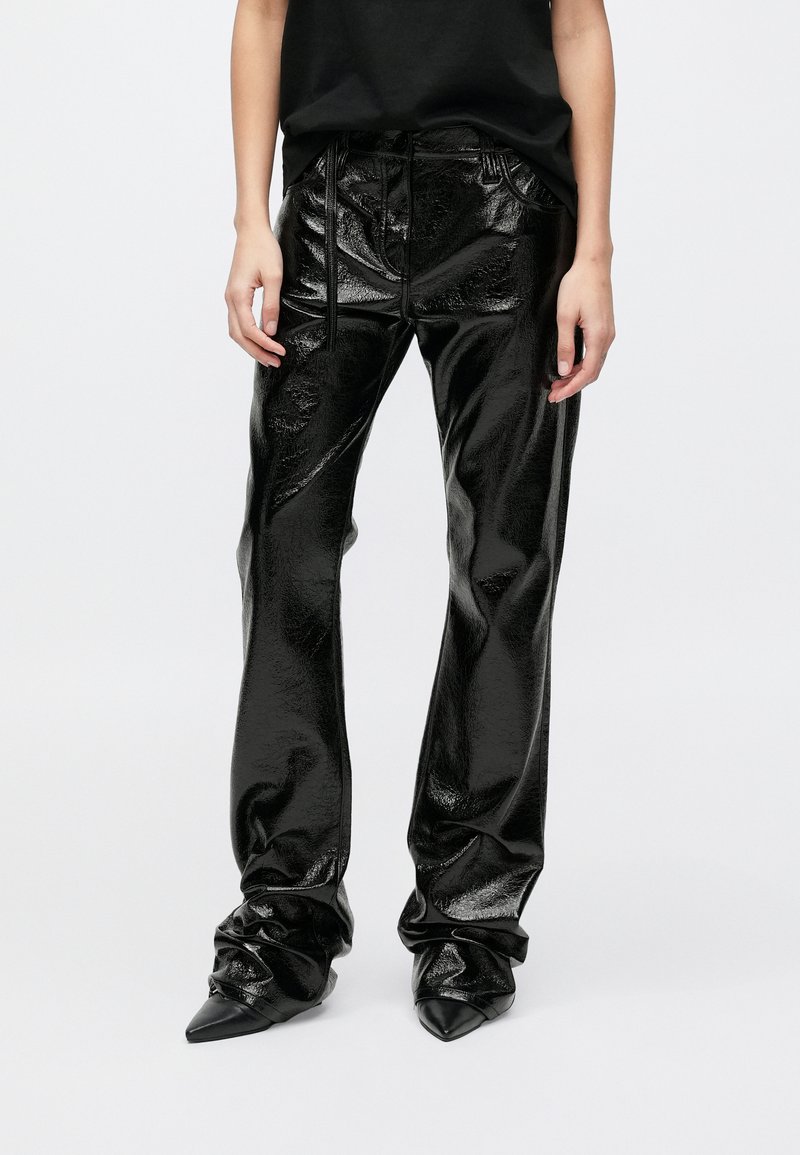 Μαύρο παντελόνι από δερμάτινο λάκα με γυαλιστερή υφή, χαλαρή εφαρμογή, μέση με κορδόνι και σούρες στα μανσέτα. Μαύρα μυτερά τακούνια.
