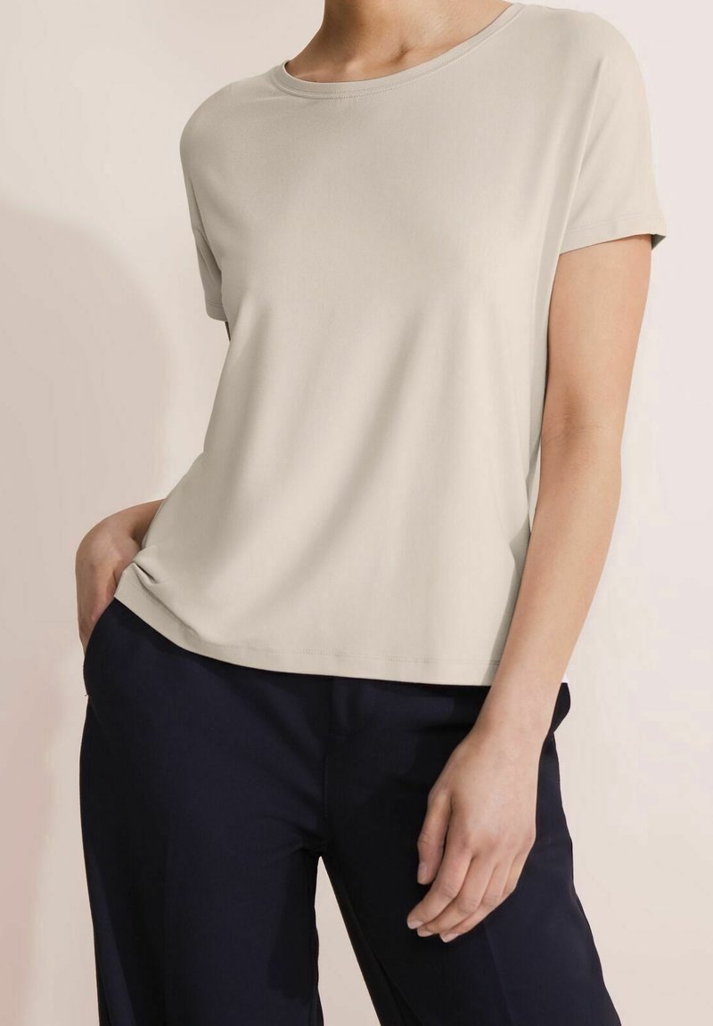 Ljusbeige kortärmad skjorta med rund halsringning, mjuk textur och avslappnad passform, i kombination med mörk marinblå byxor.