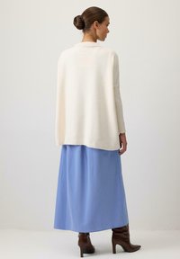 Kremīga adīta džemperis ar atvērtu aizmuguri, uzvilkts virs gaiši zilas maxi svārku. Izskats papildināts ar brūnām papēžu zābakiem.