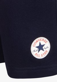 Námořnická modrá látka se šitým bílým kruhovým nášivkem s námořnickou hvězdou a červeným textem "Converse All Star Chuck Taylor."