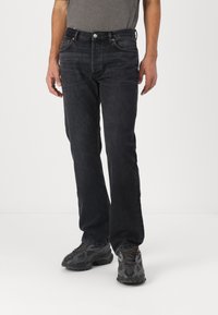 Jeans de mezclilla negra con corte recto, cinco bolsillos y costuras en contraste. Llevados con zapatillas grises texturizadas.