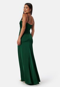 Zelené saténové večerní šaty s přiléhavým korzetem, tenkými ramínky a bočním rozparkem. Hladká textura, délka ke kotníkům a jemné detaily na zadní straně.