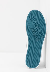 Blue rubber sneaker sole with herringbone pattern, featuring embossed "TOMMY JEANS" branding and a white outer edge.