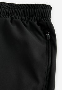 Crne atletske hlače s elastičnom trakom, glatkim materijalom i detaljima bočnog zatvarača. Imaju elegantan, uski dizajn za udobnost.