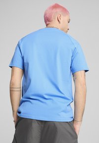 Tricou cu mânecă scurtă de culoare albastru deschis, confecționat din bumbac. Textură fină, cu decolteu rotund și tiv drept. Vedere din spate care arată cusături subtile la umeri.