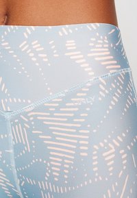 Vaaleansiniset legginsit, joissa on geometrinen kuvio vaaleanpunaista. Niissä on sileä pinta ja valkoisella ommeltu logo vyötärön kohdalla.