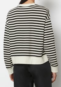 Felpa a righe in crema e nero, con collo rotondo, polsini e orlo a coste, e una vestibilità rilassata con un dettaglio di cucitura visibile sulla spalla.