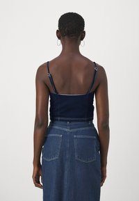 Denim top s kratkim krojem z nastavljivimi naramnicami, ki ima oprijet kroj in svetle šive. V kombinaciji z krilom iz denima visoke pasu, vidnimi zadnjimi žepi.