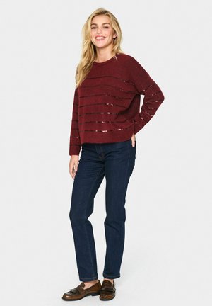 Burgundy sweater with horizontal black stripes, round neckline, and long sleeves, paired with dark denim jeans and brown loafers.