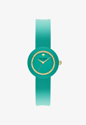 Turkis armbåndsur med gulddetaljer, rund urskive, minimale markeringer og teksten "kate spade NEW YORK" under et spar-logo.