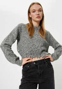Grijze cropped sweater met een gestructureerde brei, geribbelde kraag en rafelige zoom. Gecombineerd met hoge zwarte jeans.