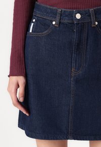 Gonna di jeans blu scuro, con design a vita media, cinque tasche, accessori in argento e cuciture arancioni a contrasto lungo le cuciture.