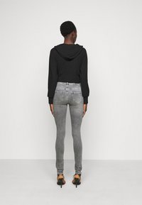 Moletom cropped preto com capuz, combinado com jeans skinny cinzentos. Os jeans têm bolsos traseiros e detalhes desgastados. Usado com sapatos de salto alto pretos.