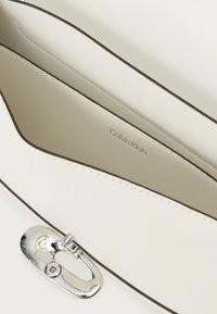 Hvid faux læder håndtaske indvendig med en lys foring, kontrasterende brun trim og en sølv metallås med logo-detalje.