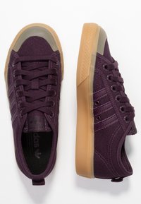 Fialové plátěné tenisky s gumovou podrážkou, průhlednou špičkou a třemi vodorovnými pruhy po straně. Součástí jsou ploché tkaničky.