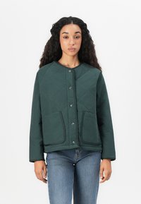 Veste matelassée verte avec un col rond, des boutons-pression et deux poches avant, fabriquée à partir d'un tissu lisse avec des coutures visibles.