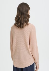 Pull en tricot rose clair avec texture côtelée, coupe ample, épaules tombantes et ourlet arrondi, vu de dos.