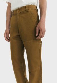 Pantalons en coton marron avec une coupe droite, dotés d'une taille avec un bouton et de poches latérales agrémentées de boutons-pression.
