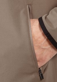 Khaki Reißverschluss-Tasche auf einem glatten Stoff. Die Tasche verfügt über einen dezenten kontrastierenden schwarzen Rand und einen Metallreißverschluss mit einem Ziehgriff.