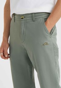 Lichtgroene broek met een gladde textuur, voorzien van een knoopsluiting, zijzakken en een subtiele geborduurde logo op de dij.