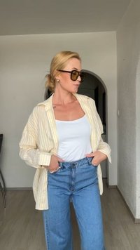 Světle žlutá a bílá pruhovaná košile přes bílý top na ramínka, spárovaná s modrými jeansy s vysokým pasem. Tmavé sluneční brýle a uhlazený účes.