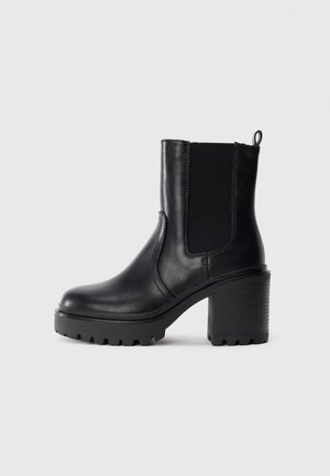 Bottine en cuir noir avec un chunky talon carré, panneau latéral élastique et une languette de tirage sur un fond clair.