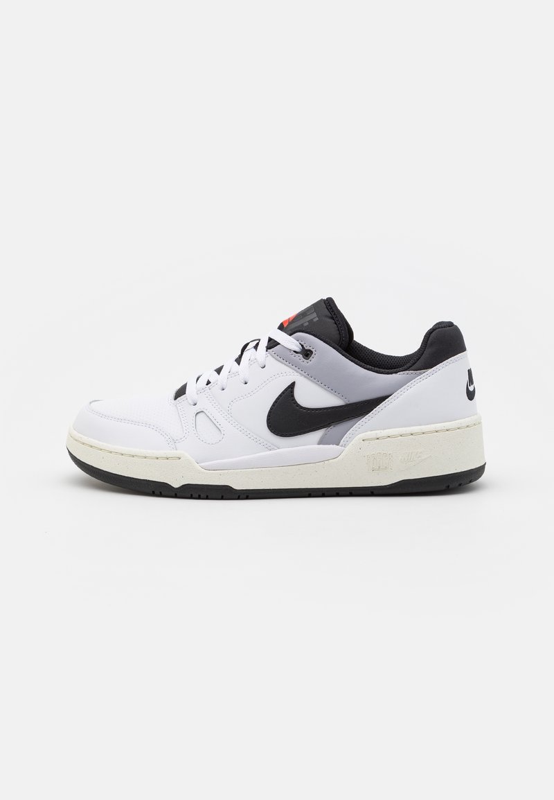 Baskets basses blanches et grises avec un logo Nike noir, un col noir, des lacets blancs et une semelle écrue sur un fond uni.