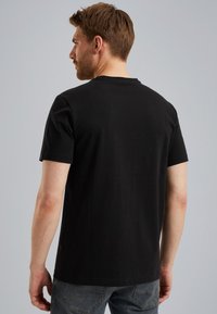 Camiseta de algodón negra con mangas cortas y cuello redondo. La vista posterior muestra líneas limpias y un diseño simple y minimalista.
