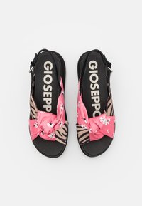 Black and beige sandals featuring a pink fabric bow with white floral patterns. Printed with a zebra motif on the sides. Brand name visible.